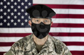 Male US soldier wearing facemask for coronavirus pandemic protection. Focus on front of mask with USA flag in background. 
