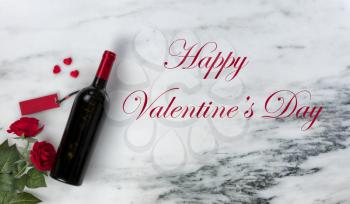 Happy Valentines Day with lovely red rose flowers and unopened bottle of red wine on natural marble stone background 