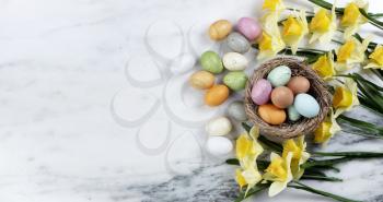 Happy Easter holiday concept with nest of colorful eggs with yellow daffodil flowers on stone background in flat lay format 