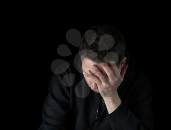 Depressed mature man holding his face in the darkness while dressed in a black sweater 