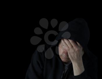 Depressed mature man holding his forehead in the darkness while dressed in a black hooded sweater 