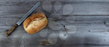Top view of homemade full sourdough loaf of bread with cutting knife on weathered wooden planks 
