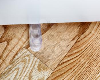 Closeup of a translucent rubber home door stopper or slider on red oak floor 