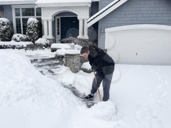 Mature man shoveling snow in front of home with snowflakes coming down 
