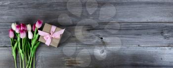 Overhead view of pink tulips and a giftbox on rustic wood for Mothers Day concept 