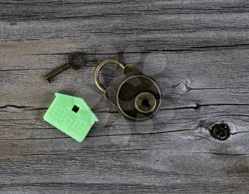 Close up of miniature house key holder with key and antique lock on vintage wooden plank background 