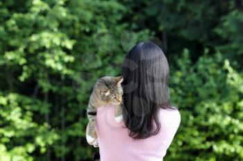 Woman holding family pet cat while outdoors with back to camera