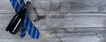 Blue striped necktie and a bottle of red wine and corkscrew opener on weathered wooden planks for Happy Fathers Day concept
