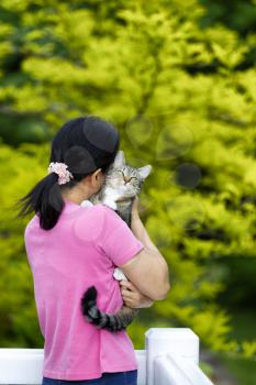 Woman hugging smug looking family pet cat while on outdoor home deck with back to camera
