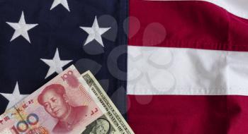 Waving cloth US flag with Chinese yuan and American currency in lower left corner for Trade War Concept 