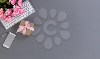 Desktop workspace with computer keyboard, giftbox, smartphone and lovely pink rose flowers in flat lay top view with plenty of copy space available for Mothers Day holiday concept 
