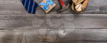 Fathers day top border concept with blue dress tie, hammer, baseball items and a gift box on rustic wooden background in flat lay format