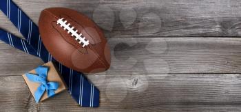 Fathers day concept with blue dress tie, American football and a gift box on rustic wooden background in flat lay format