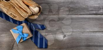Fathers day concept with blue dress tie, baseball items and a gift box on rustic wooden background in flat lay format