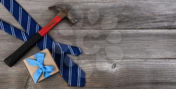 Fathers day concept with blue dress tie, hammer and a gift box on rustic wooden background in flat lay format