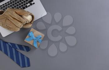 Fathers day concept with blue dress tie, baseball glove, giftbox and laptop computer on a gray background in flat lay format