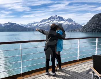 Mother holding her daughter while pointing out mountains and glaciers on Alaska tour via ship 