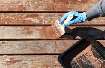 Gloved hand working in stain on home outdoor wooden cedar deck boards