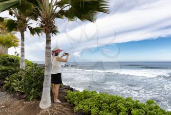 Woman taking photo of ocean and sky while under a palm tree in Hawaii
