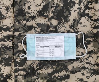 Covid 19 vaccination record card and personal facemask on military uniform.  Individual record for use during the covid 19 coronavirus global pandemic 