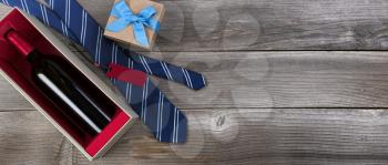 Fathers day concept with blue dress tie, red wine bottle and a gift box on rustic wooden background in flat lay format