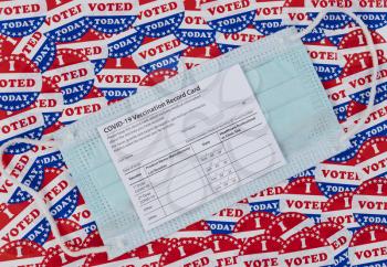 Covid 19 vaccine record card positioned on top of I voted today stickers background with United States national colors or red, white and blue for legal requirements 