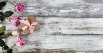 Real pink rose flowers and giftbox on left side of rustic wooden planks for mothers day or valentines holiday 