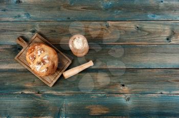 Freshly baked whole loaf of sourdough, flour, rolling pin and server on faded blue wooden planks in flat lay format