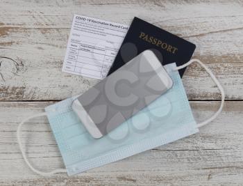 Covid 19 vaccination record card, US Passport, facemask and smartphone in close up format  
