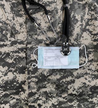 Covid 19 vaccination record card, personal facemask and stethoscope on military uniform.  Individual record for use during the covid 19 coronavirus global pandemic 