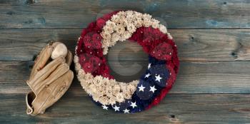 Wreath with United States national colors of red, white and blue with stars plus baseball glove and ball on faded blue wooden planks for happy memorial or Independence Day background concept 