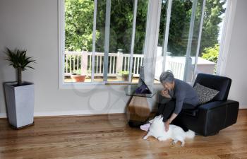 Senior woman talking on smartphone while petting her family dog at home 