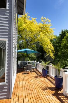 Vertical view of home outdoor wood cedar deck with trees in full seasonal color along with furniture and palm tree plants 