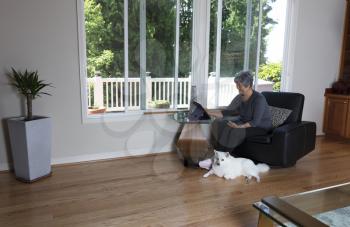 Senior woman looking at her computer while family dog laying near her side at home  