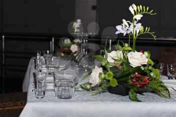 Flower composition of freesia, roses and hypericum on tables set for dining