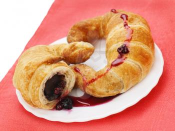 fresh and tasty croissants with chocolate and raspberry jam on plate on red background