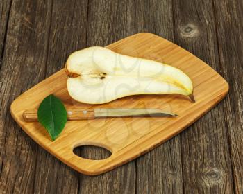 Half of pear and knife on wooden background. Closeup.
