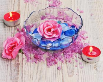 Soap in form of roses in bowl of water on wooden background. Closeup.