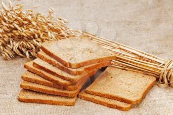Chunks of bread and ears of rye on natural background. Closeup.