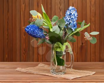 Bouquet from tulips and hyacinths in glass vase on wooden background.