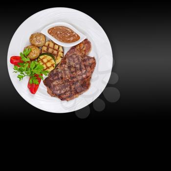 Grilled steak, baked potatoes and vegetables on white plate on black background.