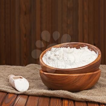 Flour in wooden bowl on nature background. Closeup.