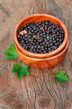 Sweet, black currant and green leaves in wooden bowl. Closeup. Selective focus.