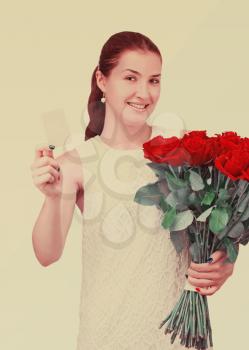 Young beautiful girl in white dress with bouquet of red roses and business card in hand with retro effect filter.
