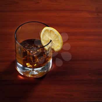 Highball whiskey glass with ice and lemon on wooden background. Closeup.