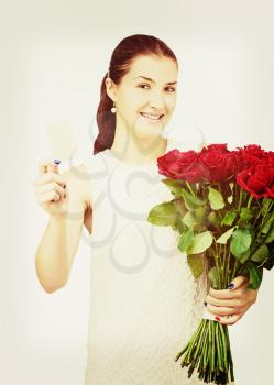 Young beautiful girl in white dress with bouquet of red roses and business card in hand with retro effect filter.