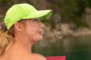 Outdoors portrait of pretty blonde woman in green baseball cap posing on background of  sea coast.  Closeup.