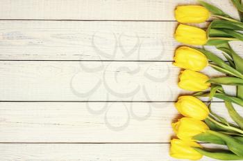 Fresh yellow tulips on wooden background. Holiday background. Top view. Photo with retro filter effect.