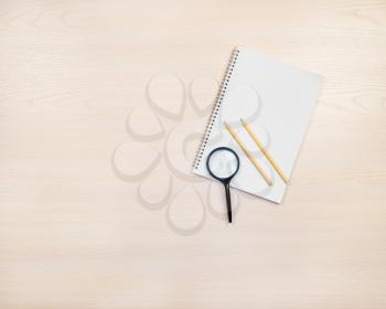 Magnifying glass, pencils and notepad on light сoloured wooden background.