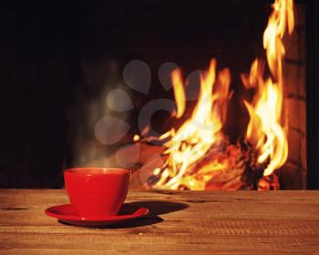 Red cup of tea or coffee near fireplace on wooden table. Winter and Christmas holiday concept. Photo with retro filter effect.